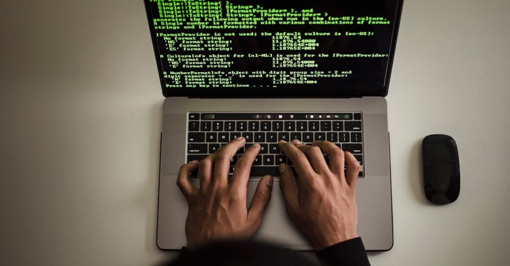 From above crop anonymous male programmer in black hoodie working on software code on contemporary netbook and typing on keyboard in workspace